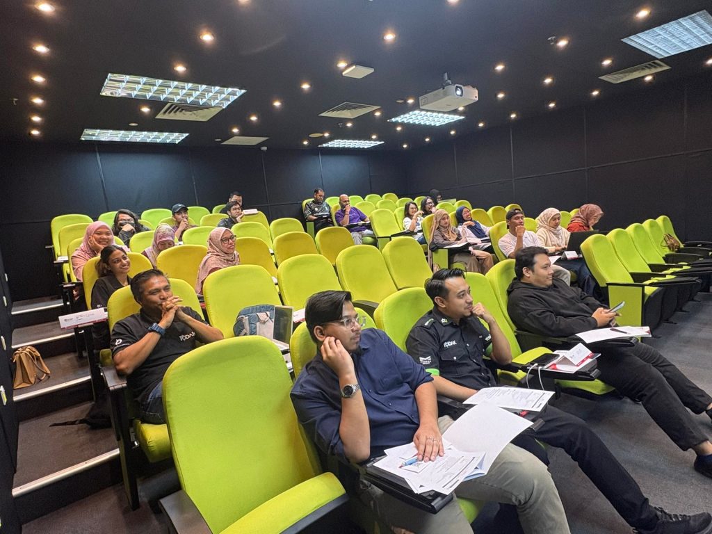 Participants seated in a tiered training room with notes in hand