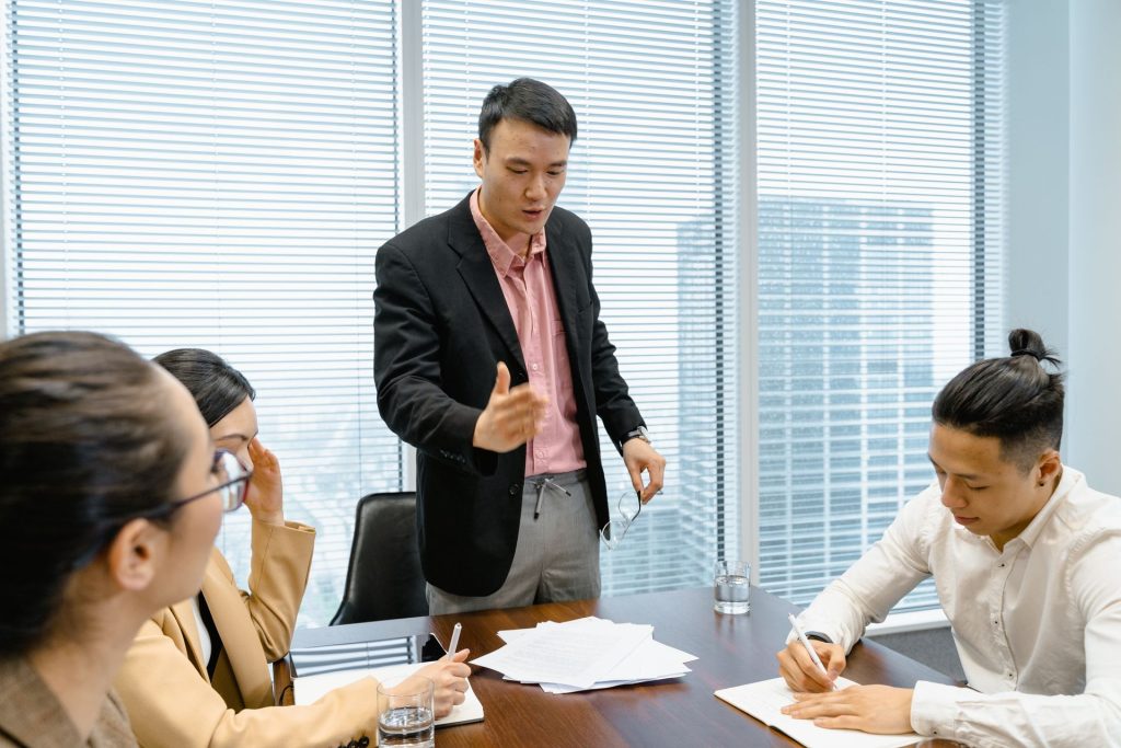 Man standing and speaking to seated colleagues at a meeting table