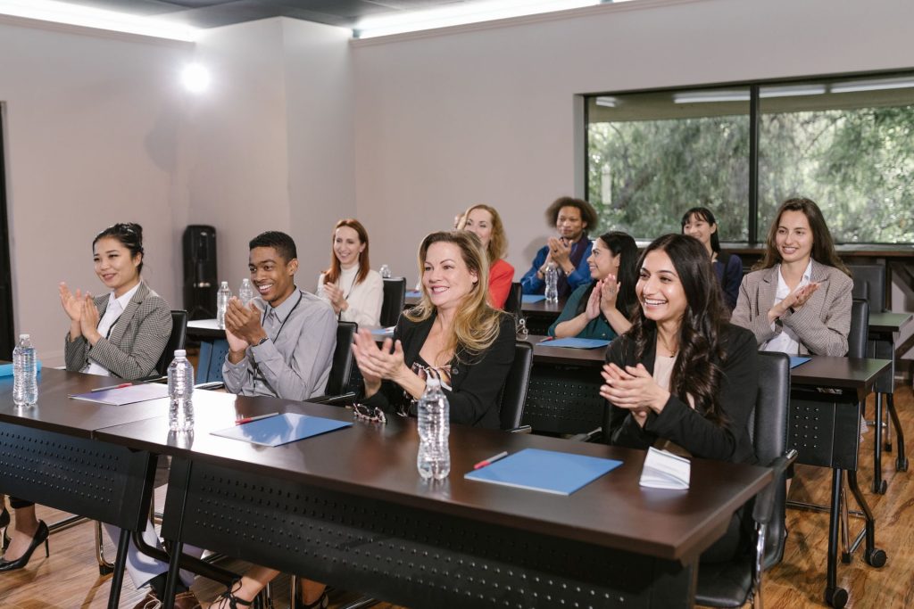 Participants seated at long tables in a training room, applauding