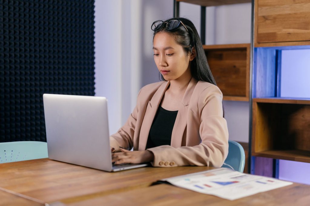 Woman typing on a laptop at a desk with printed charts